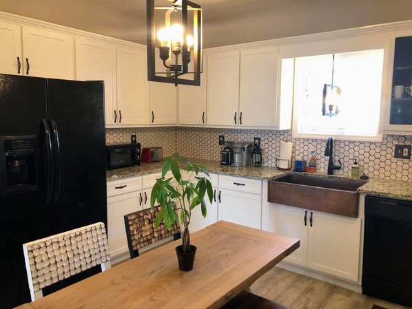A modern kitchen with white cabinets, a black refrigerator, a coffee machine, and a potted plant on the counter.