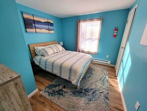 Ein Schlafzimmer mit Bett, einem Fenster mit Vorhängen, einem Feuerlöscher und einer blauen Wand.