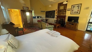 A hotel room with a bed, a desk, a chair, a television, a fireplace, and a view of the outdoors. - Two Creeks School House (Forest Reefs)