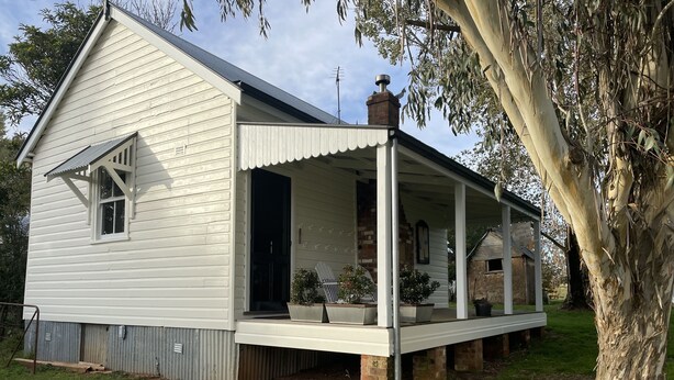 A white two-story house with a covered porch and a brick chimney. - Two Creeks School House (Forest Reefs)