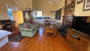 A spacious living room with a wooden floor, a green patterned sofa, a television, and a kitchen area in the background. - Two Creeks School House (Forest Reefs)