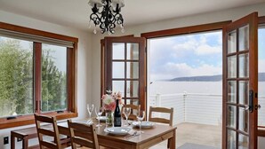 Een eetgedeelte met een houten tafel voor vier personen, een kroonluchter en grote ramen met uitzicht op zee.
