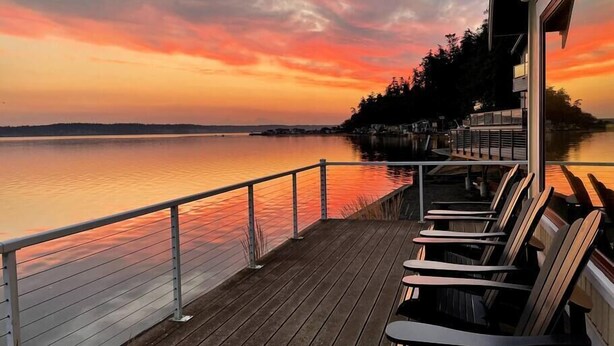 Een houten terras met stoelen met uitzicht op een kalm wateroppervlak tijdens de zonsondergang.