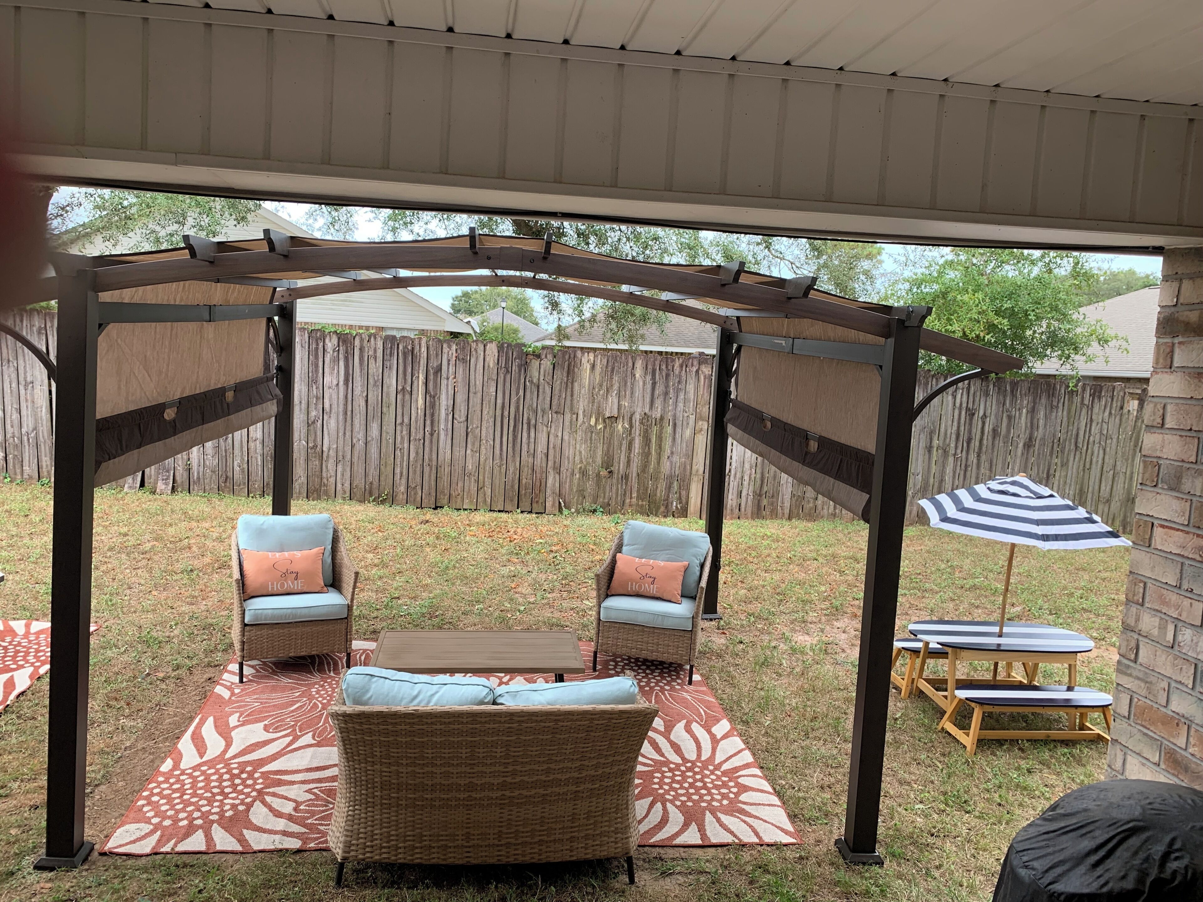 A covered patio area with wicker furniture, a wooden table, and a striped umbrella.