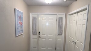 A hallway with a dark wooden floor, white doors, and a painting of flamingos on the wall.