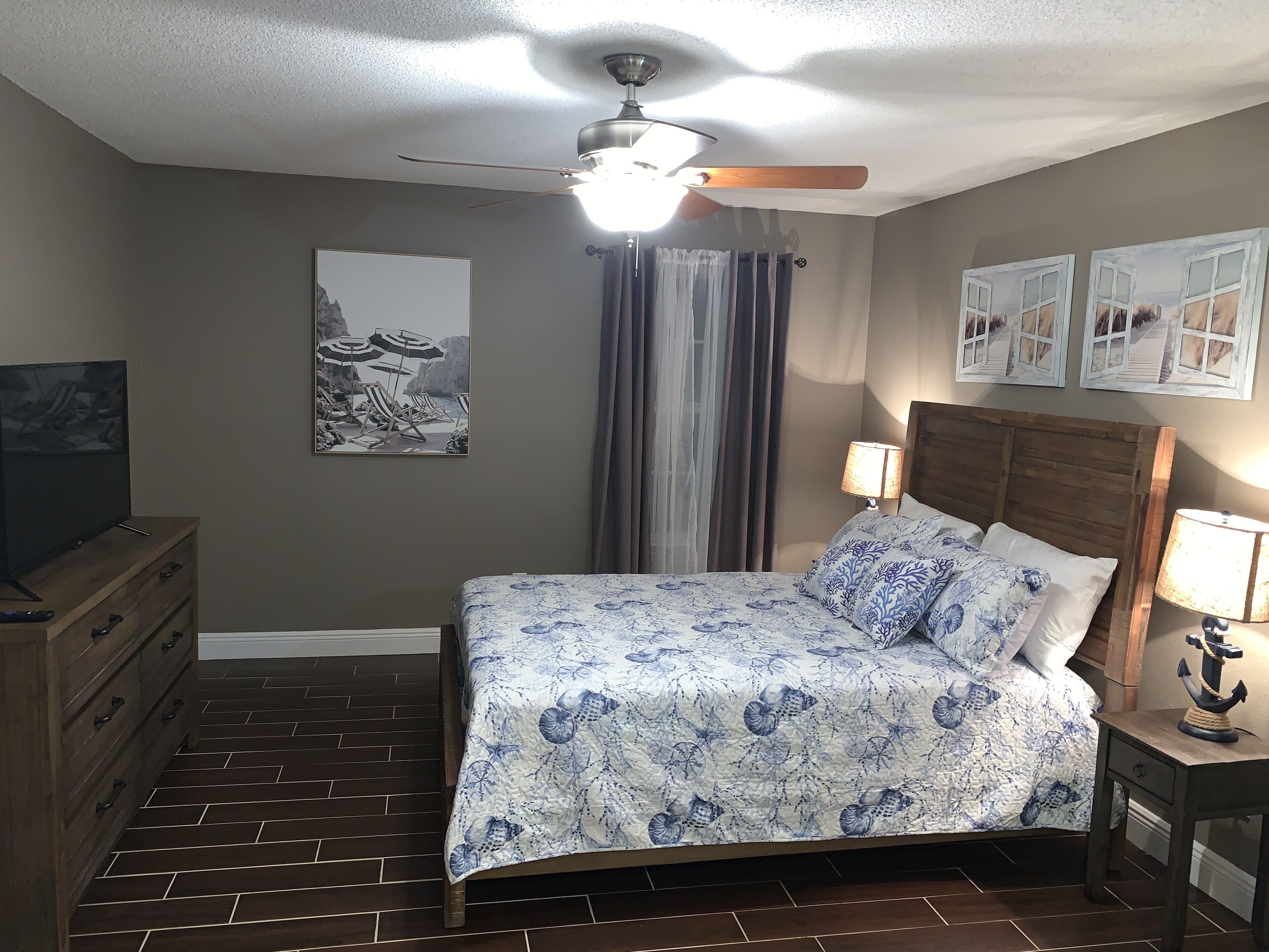 A bedroom with a bed, a ceiling fan, a TV, and a dresser.
