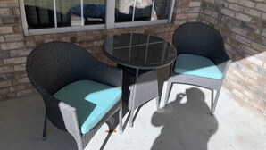 A patio area with wicker chairs and a glass table, a brick wall, and a window with blinds.