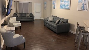 A living room with a grey sofa, a white armchair, and a TV mounted on the wall.