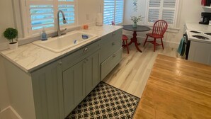 A modern kitchen with a marble countertop, a sink, and a dining area with a wooden table and red chairs. - Chic cottage, Vamo area, close to beaches, pet friendly, kayaks, large backyard  (Sarasota)