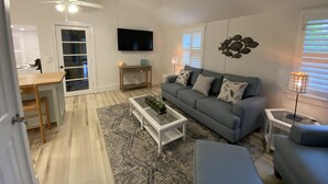 A living room with a grey sofa, a coffee table, a TV mounted on the wall, and a ceiling fan. - Chic cottage, Vamo area, close to beaches, pet friendly, kayaks, large backyard  (Sarasota)