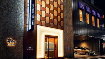 A hotel entrance with a modern design, featuring a patterned facade and illuminated signage.