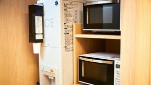 Et kompakt køkken med køleskab, mikroovn og kopdispenser.