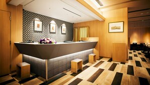 Et hotellets reception område med et moderne design, inklusive en receptionsdisk, siddeområde og indrammede kunstværker på væggene.