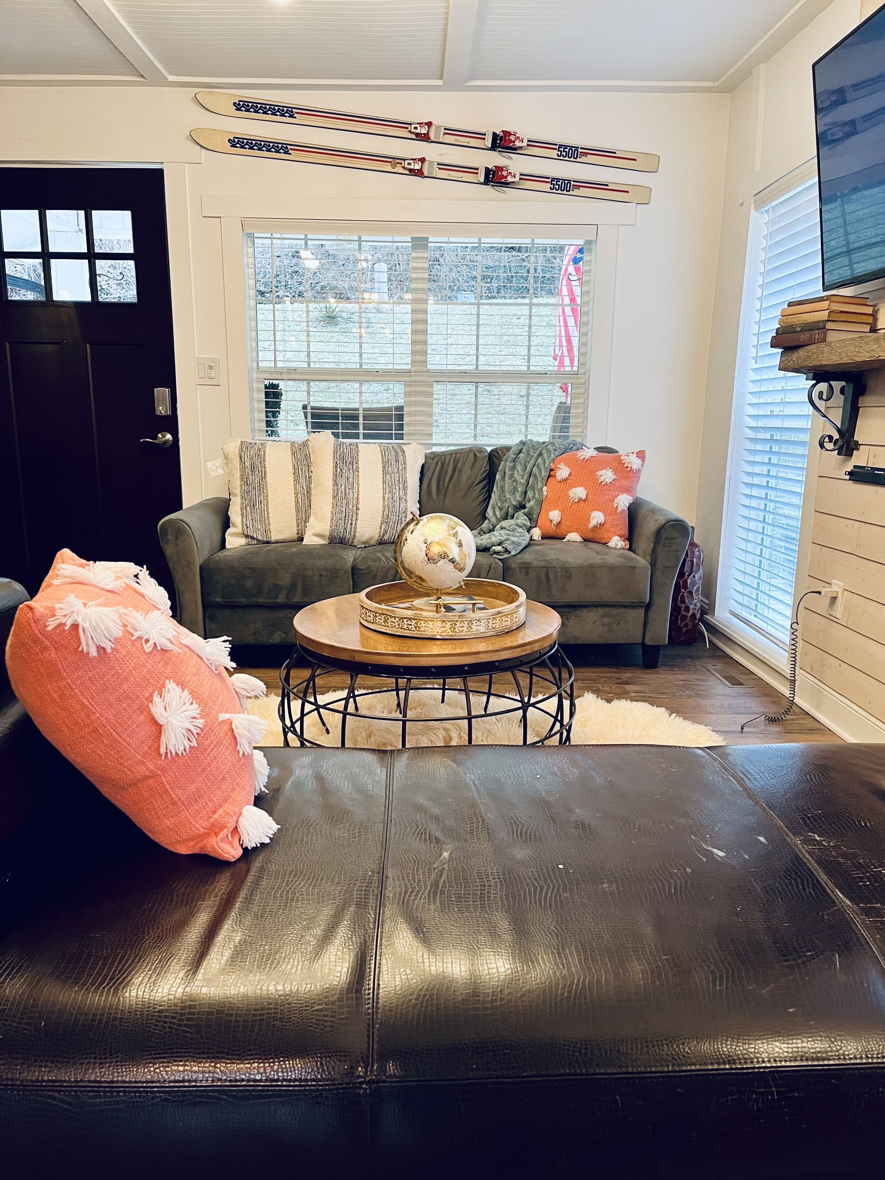 A living room with a dark leather sofa, a round coffee table, and a window with blinds.