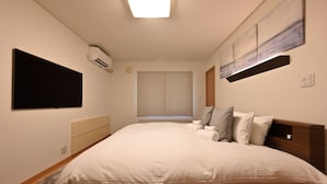 A modern hotel room with a large bed, a flat-screen TV mounted on the wall, an air conditioning unit, and a painting above the bed. - Casi 15 (Furano)