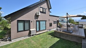 A modern two-story house with a deck, large windows, and an air conditioning unit. - Casi 15 (Furano)