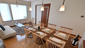 A dining area with a wooden table set for six, surrounded by wooden chairs. There is a sofa and a small table with a chair in the background. - Casi 15 (Furano)