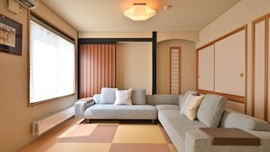 A modern living room with a sofa, tatami mat flooring, a ceiling light fixture, and a sliding door. - Casi 15 (Furano)