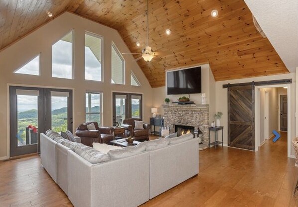 A spacious living room with a large sectional sofa, a fireplace, and a TV mounted on the wall.