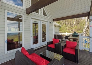 A covered outdoor area with wicker furniture and red cushions, a grill, and a view of the surrounding landscape.