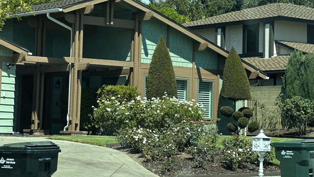 Una casa de dos pisos con un porche delantero, un pequeño jardín con flores y un buzón.