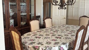 Un comedor con mantel floral, sillas de madera, una araña y un aparador.