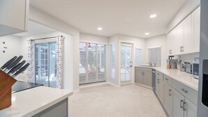 Une cuisine moderne avec des armoires blanches, un plan de travail en marbre et une vue à travers la porte vitrée.