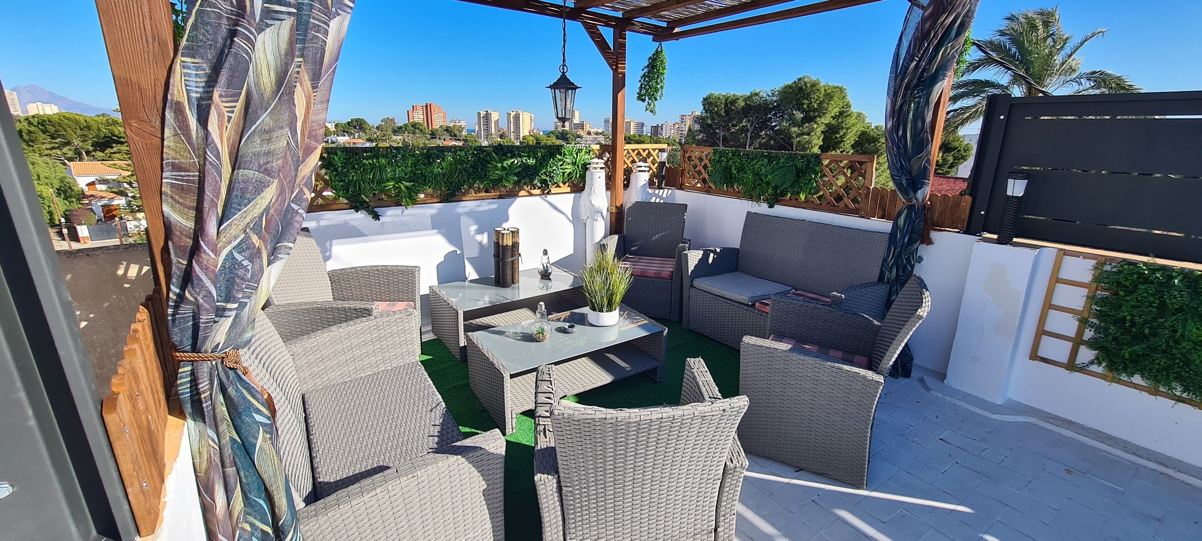 A covered outdoor seating area with wicker furniture, a table, and a potted plant.
