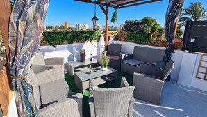 A covered outdoor seating area with wicker furniture, a table, and a potted plant.