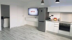 A modern kitchen with white cabinetry, a built-in oven, and a refrigerator. A flat-screen TV mounted above the refrigerator displays the Netflix logo.