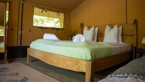 A wooden bed with a green bedspread and white pillows in a room with yellow walls and a window with a curtain.