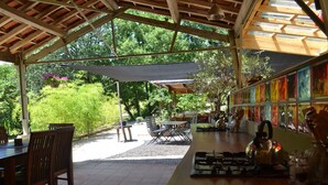 An outdoor dining area with wooden tables and chairs, a gas stove, and a view of greenery.