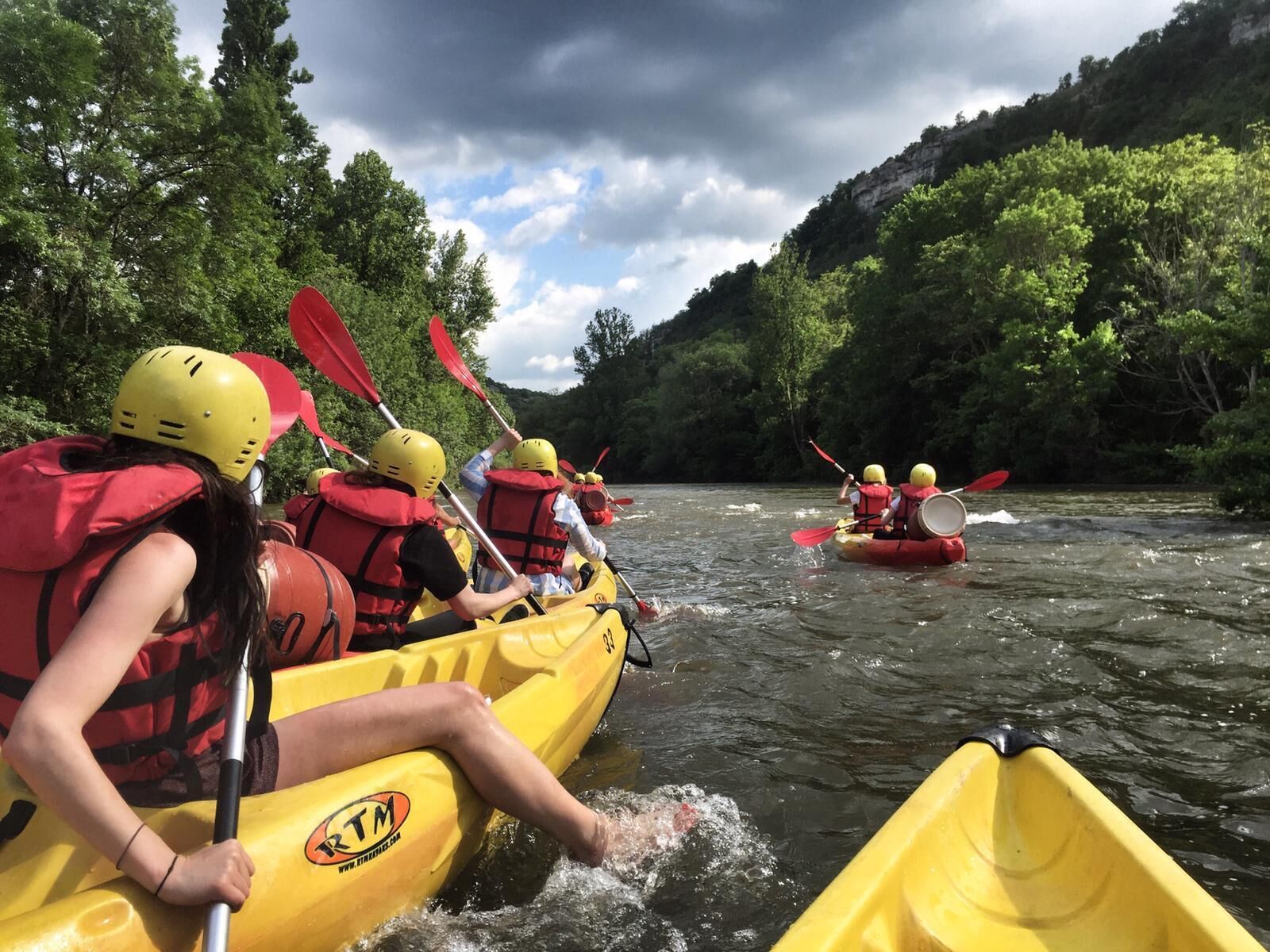 A group of people in yellow kayaks on a river surrounded by greenery.