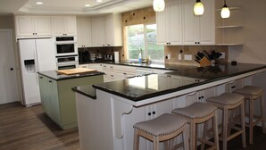 A modern kitchen with white cabinets, a large island with stools, built-in appliances, and pendant lighting. - Relaxing Mountain View Retreat with Pool & Spa! (Bonita)