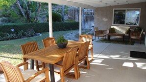 A covered patio with a wooden table and chairs, a potted plant, and a view of a garden with a waterfall. - Relaxing Mountain View Retreat with Pool & Spa! (Bonita)