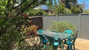 Un patio con mesa y sillas, rodeado de diversas plantas y árboles.
