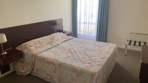 Una habitación de hotel con una cama grande, una mesita de noche, una lámpara, una ventana con cortinas y una silla.