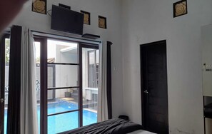 A hotel room with a bed, a TV mounted on the wall, and a sliding glass door leading to a pool area.