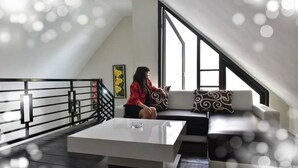 Ett modernt rum i loftstil med ett stort fönster, en vit soffa med mönstrade kuddar och ett soffbord i glas.