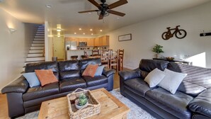A spacious living area with two black leather sofas, a wooden coffee table, and a ceiling fan. A kitchen is visible in the background with wooden cabinets and a microwave. - New!  Beautiful, secluded views 10 minutes from Downtown Moab!  (Moab)