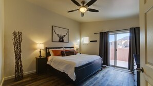 A bedroom with a bed, a ceiling fan, a wall-mounted artwork, a nightstand, a lamp, and a view through a sliding door to an outdoor area. - New!  Beautiful, secluded views 10 minutes from Downtown Moab!  (Moab)