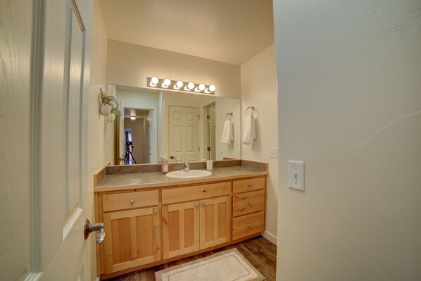 A bathroom with a vanity, a large mirror with lights, wooden cabinets, and a door. - New! Beautiful, secluded views 10 minutes from Downtown Moab! (Moab)