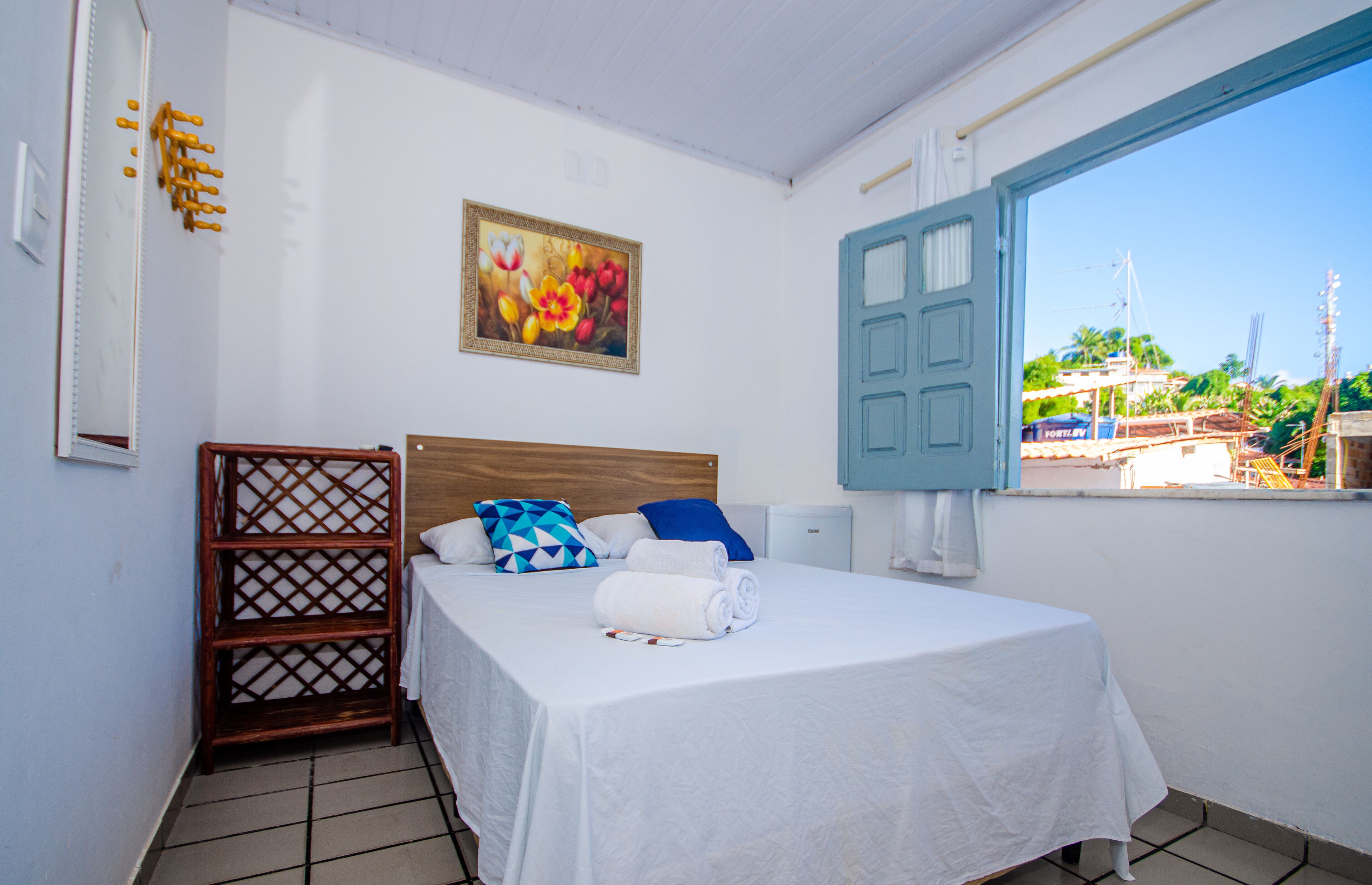 Habitación de hotel con una cama, estante de madera, un cuadro y vistas al exterior.