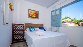 Habitación de hotel con una cama, estante de madera, un cuadro y vistas al exterior.