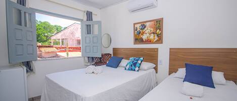 Habitación de hotel con dos camas, una ventana con cortinas, un cuadro en la pared y un aire acondicionado.