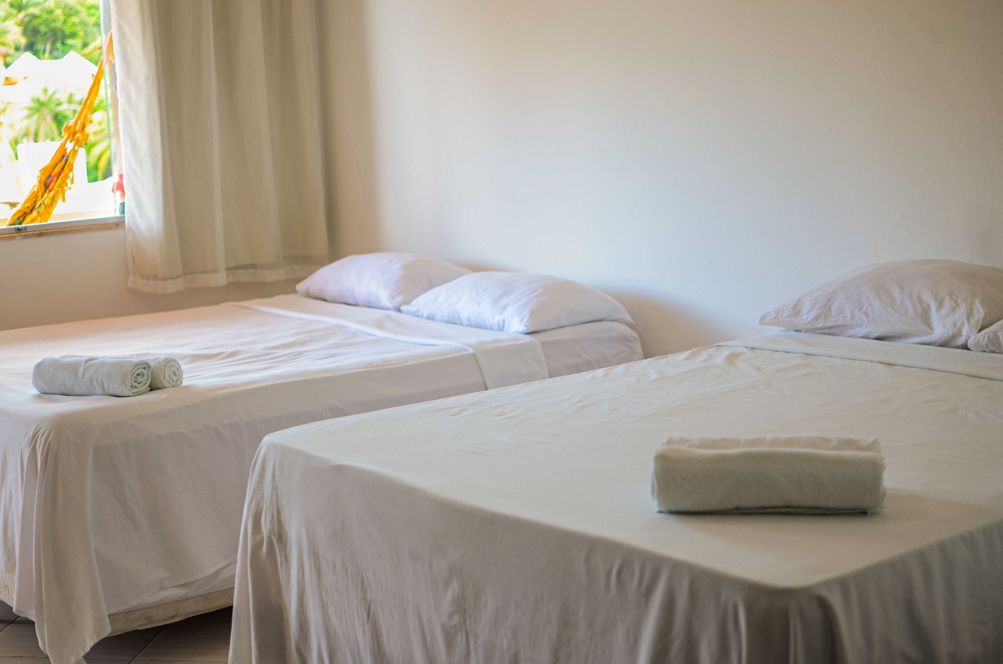 Quarto de hotel com duas camas individuais, cada uma com uma toalha branca dobrada.