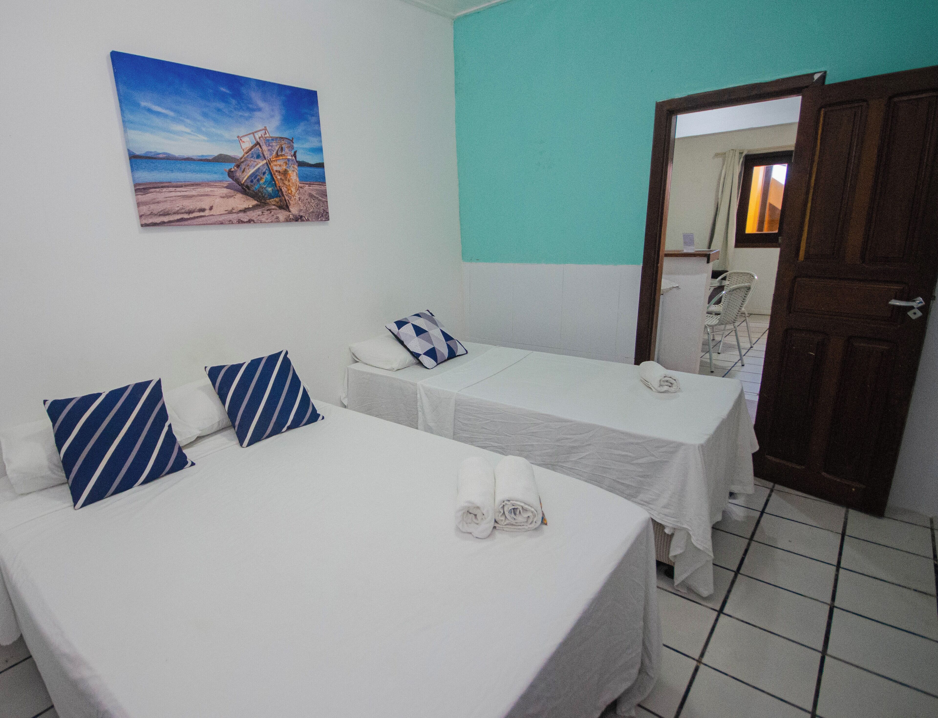 A hotel room with two beds, each with a white bedspread and blue striped pillows. There is a painting of a boat on the wall, and a door leading to another room.