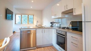 A modern kitchen with stainless steel appliances, white cabinets, and a window providing natural light. - Snow Dayz - Dinner Plain (Dinner Plain)