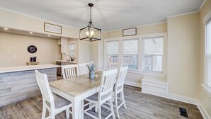 Un espace repas avec une table en bois et des chaises blanches, un coin café et un luminaire suspendu.