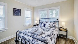 Une chambre à coucher comprenant un lit, deux tables de chevet, un ventilateur de plafond et une fenêtre avec des stores.